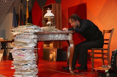 Schauspieler sitzt gebeugt an einem Tisch auf der Bühne