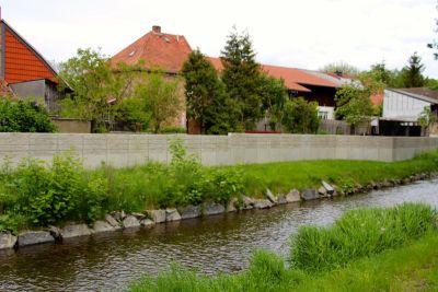 Der Fluß Ilse. Am Ufer eine hohe Betonwand, dahinter Wohnhäuser.