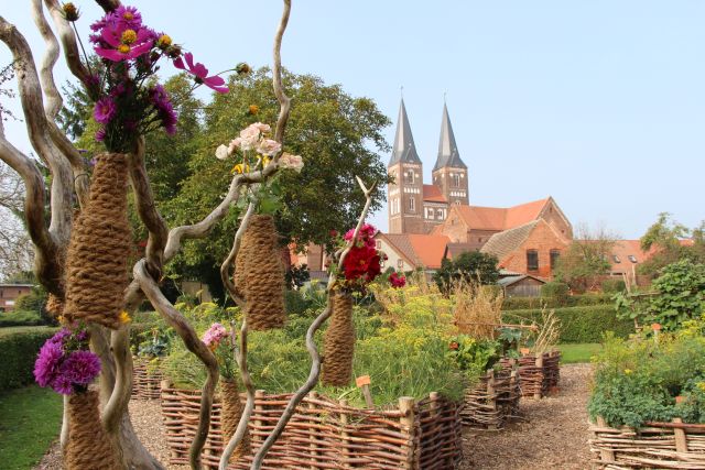 Im Klostergarten. Blumenbewachsene Beete, mit Weidengeflecht umrandet.