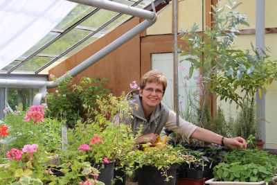 Dr. Andrea Finck steht im Gewächshaus zwischen Kräutern und Geranien.