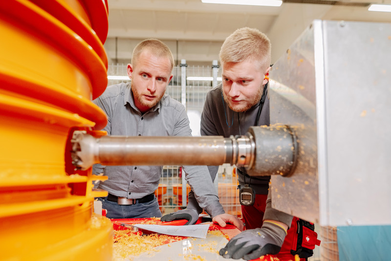 Das Foto zeigt zwei Personen an einer Produktionsanlage. 