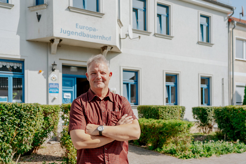 Das Bild zeigt Ulrich Weimeister, Vorsitzender und Leiter des Europa-Jugendbauernhofes, vor dem Haus. 