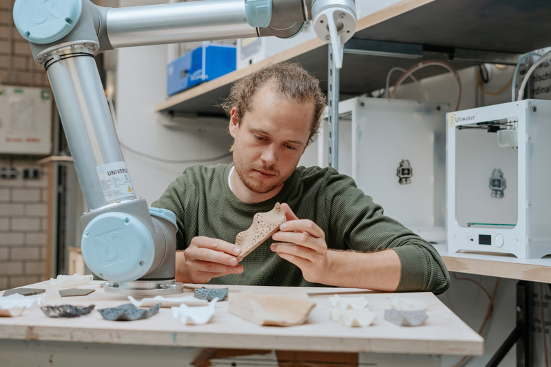 Das Foto zeigt einen Mann an einem Roboter, der Designentwürfe in der Hand hält.